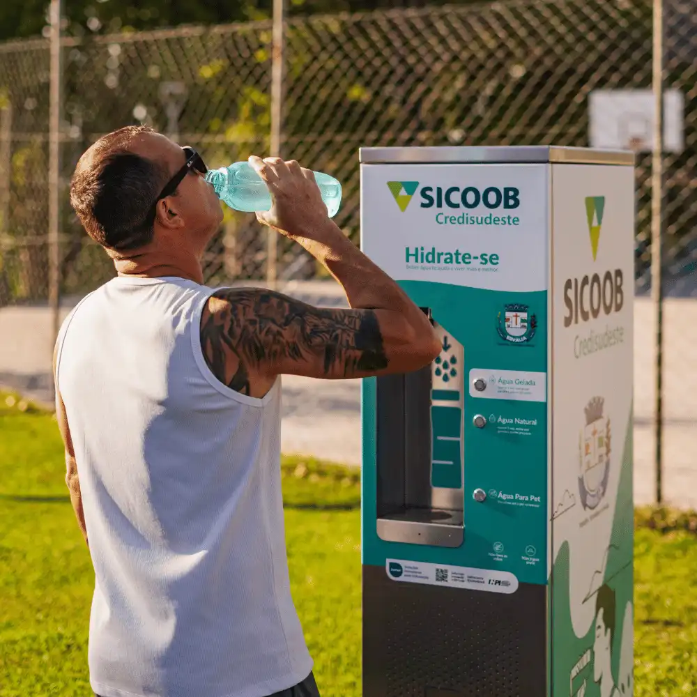 Homem bebendo água ao lado de uma estação Sicoob