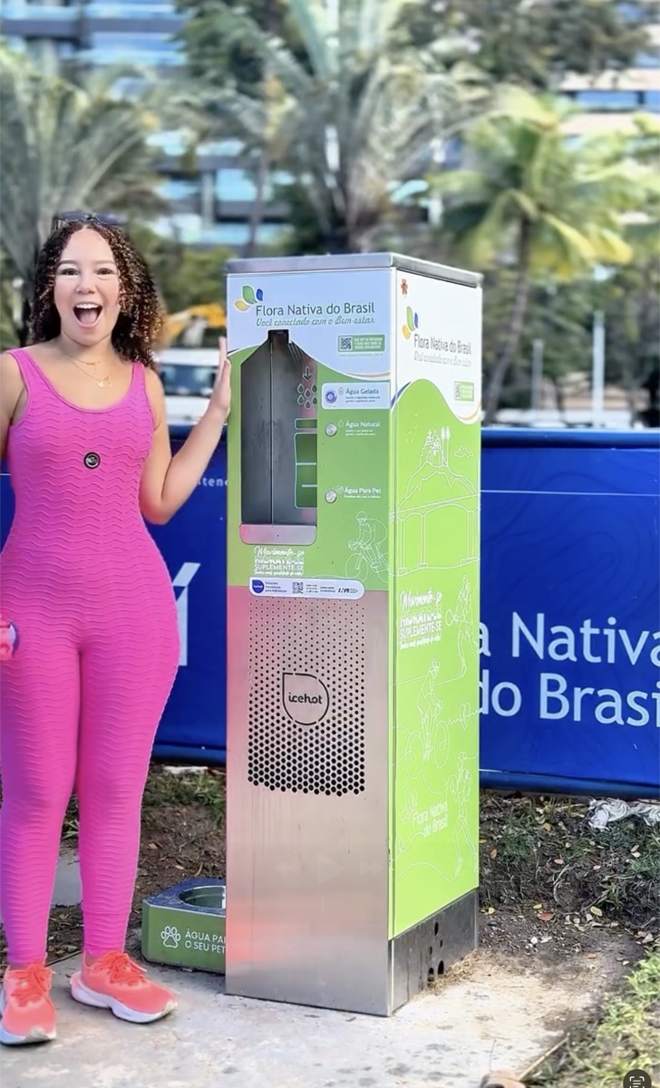 Pessoa sorrindo ao lado de estação Icehot personalizada com a marca Flora Nativa do Brasil em espaço público